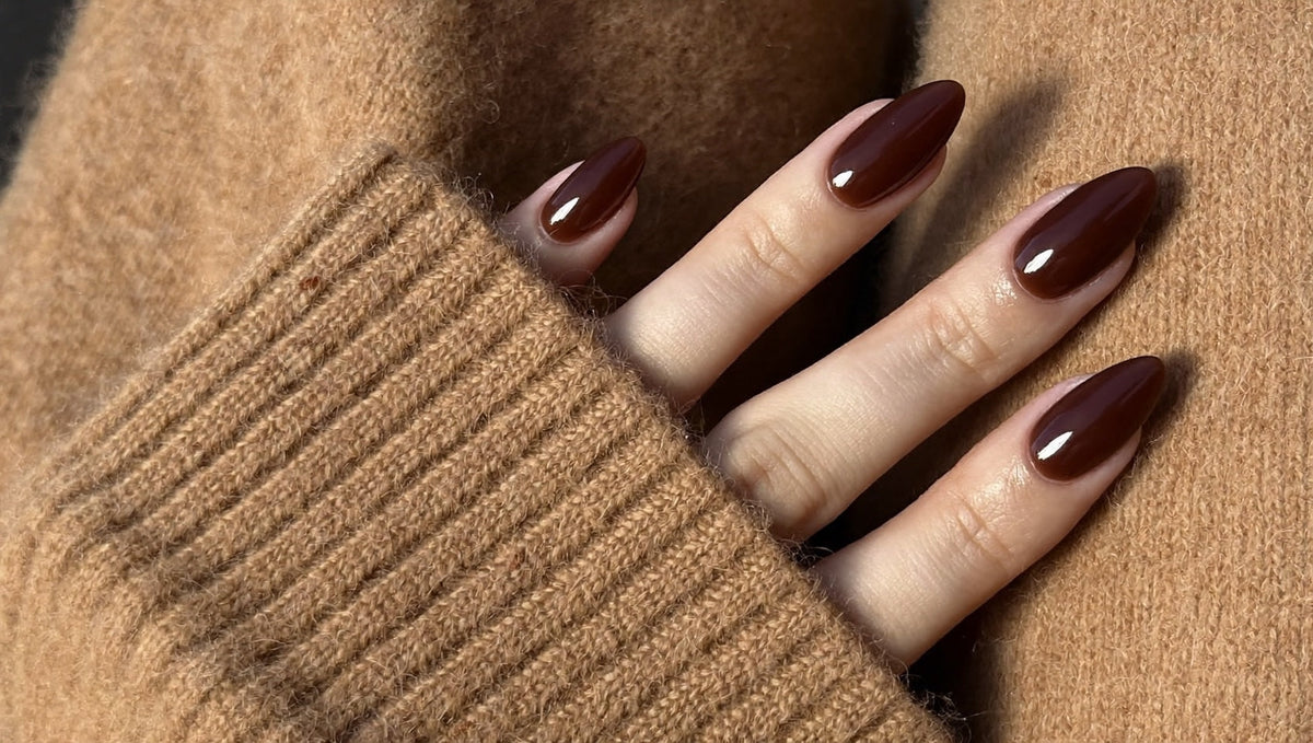 Hand with glossy dark chocolate brown almond nails resting on a camel cashmere sweater