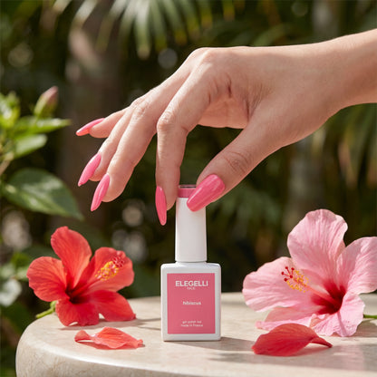 Hand with pink nail polish holding a bottle of ELEGELLI nail polish with flowers in the background